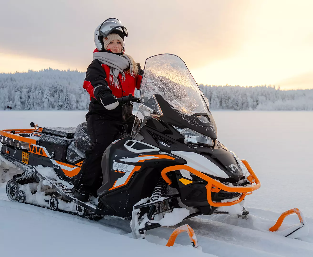 Nainen moottorikelkan selässä auringonlaskussa lumisen järven jäällä